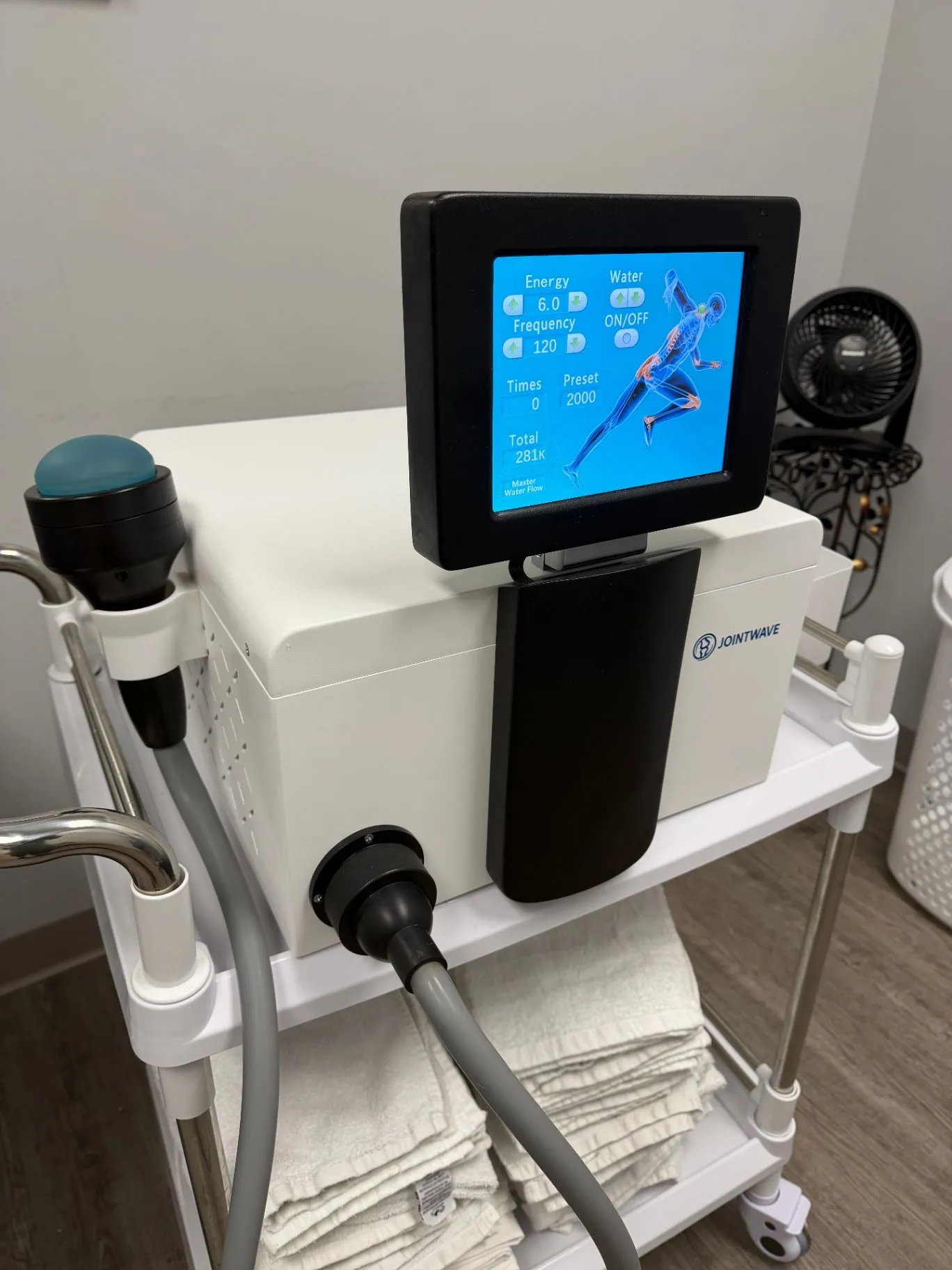 JointWave system on its mobile cart with the handpiece and touchscreen ready for use
